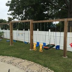 an empty playground with swings and toys in the grass near a white fenced area