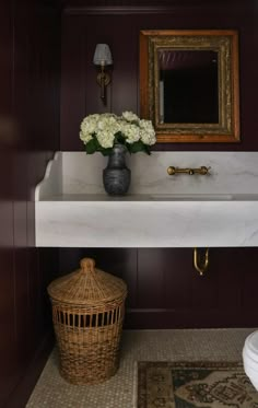 a white sink sitting under a mirror next to a wooden basket with flowers in it