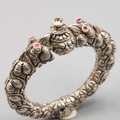 Makara silver bracelet from South India (Madras) - True Ethnic Jewelry - Mininga jewlery - Rare tribal bracelet from India ✓. made with high grade silver ✓. weight: 138 grams ✓.  internal diameter (widest): 4,6 cm (1.8 inches) This superb bracelet is antique, first half of the 20th century. It was made in India. It consists of two parts joined by a hinge. The bracelet is held closed by a screw. The bracelet is adorned with 2 Makara heads (a mythical Indian animal) whose wide-open mouth is biting Luxury Silver Meenakari Bracelet, Indian Animals, Open Mouth, South India, The 20th Century, Ethnic Jewelry, Red Glass, Green Stone, Arm Band