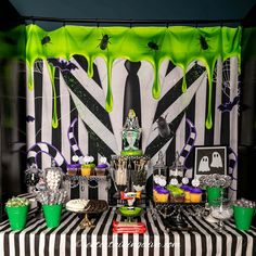 a table topped with cupcakes and cakes covered in green icing next to a black and white striped wall