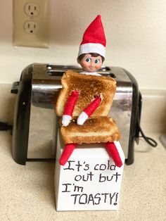 an elf is sitting on top of a toaster and holding a sign that says it's cold out but i'm toasty