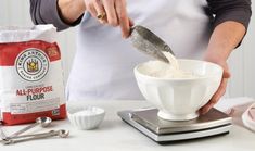 a person in an apron is mixing flour into a bowl with a measuring scale on the counter