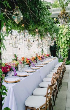 a long table is set with white linens and flowers on it for an outdoor dinner