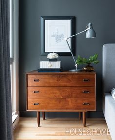 a bedroom with grey walls and wooden dresser in the foreground, framed artwork on the wall