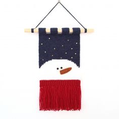 a knitted snowman hanging on a wall with red fringes and a blue scarf