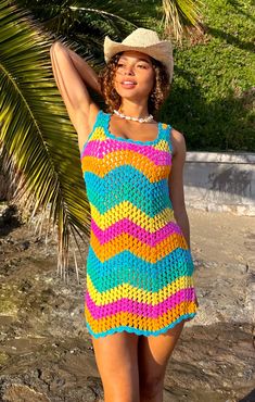 a woman in a colorful crochet dress and hat posing for the camera with her arms behind her head