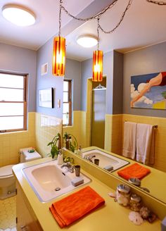 a bathroom with yellow walls and orange towels hanging from the ceiling, along with two sinks