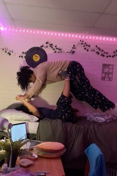 two people jumping on top of a bed in a room with pink walls and purple lights