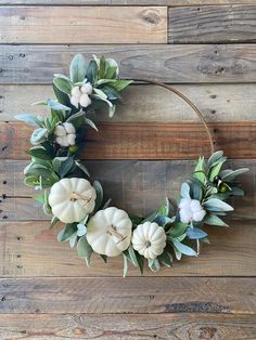 a wreath with white pumpkins and greenery on a wooden background, ready to be used as a decoration