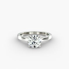 a white gold engagement ring with a round brilliant cut diamond in the center, on a plain background