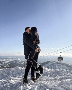 a man and woman standing on top of a snow covered slope next to a ski lift