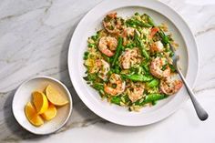 a white plate topped with shrimp and asparagus next to a bowl of lemon wedges