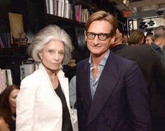 two people standing next to each other in front of a book shelf with books on it