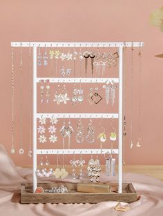 a white jewelry rack with earrings and necklaces hanging from it's sides on a pink background