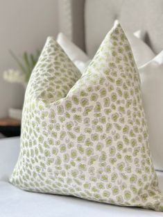 two pillows sitting on top of a bed with white sheets and green spots in them