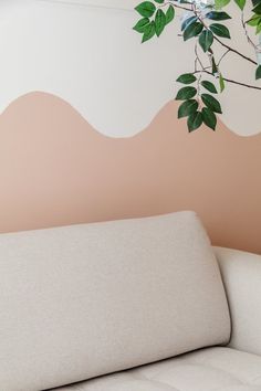 a white couch sitting in front of a wall painted with pink and green leaves on it