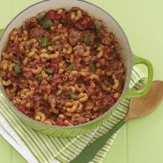 a pot filled with pasta and meat sitting on top of a green towel next to a wooden spoon