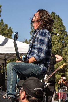 a man sitting on top of a guitar in front of a microphone and other people