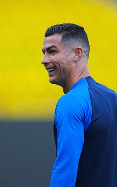 a close up of a person wearing a blue shirt and smiling at the camera with a yellow wall in the background