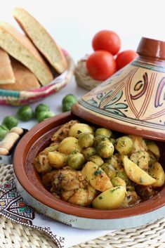 a bowl filled with potatoes and vegetables next to bread on a tablecloth covered place mat