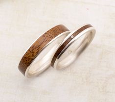 two silver rings with wood inlays on them sitting on a table next to each other