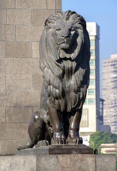 a statue of a lion in front of a cityscape with tall buildings behind it