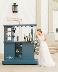 a woman in a wedding dress standing next to a blue bar with bottles on it