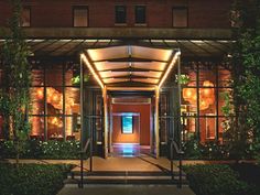 the entrance to an apartment building lit up at night with lights and plants on either side