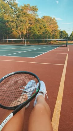 a person holding a tennis racquet on top of a tennis court with trees in the background