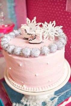 a pink frosted cake with snowflakes on top and decorations around the edges