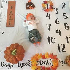 a baby laying on top of a white blanket next to fall leaves and pumpkins