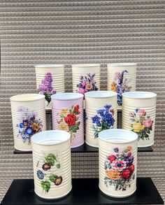 several white buckets with flowers painted on them sitting on a black shelf in front of a wall