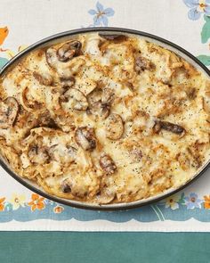 a casserole dish with mushrooms and cheese on a floral tableclothed placemat