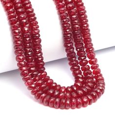 three strands of red glass beads on a white surface with one strand in the middle