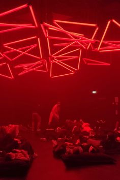 a room filled with lots of people laying on the floor and some red lights hanging from the ceiling