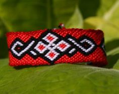 a red and black beaded bracelet sitting on top of a green leaf