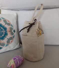 a small bag sitting on top of a couch next to a pillow and knitting needles