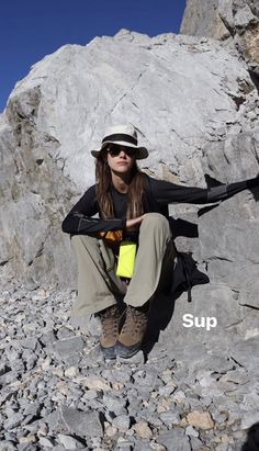 a woman sitting on top of a pile of rocks wearing a hat and holding a yellow item