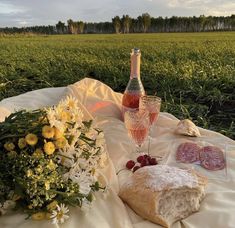 a bottle of wine, bread and flowers on a blanket in the middle of a field