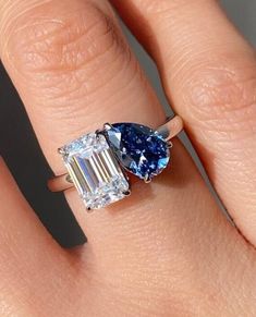 a woman's engagement ring with two pear shaped blue and white diamonds on it