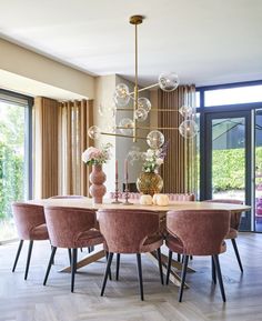 a dining room table with pink chairs and chandelier in front of large windows