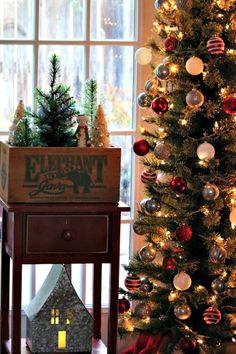 a small christmas tree in front of a window with a lit house on the side