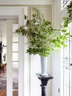 a tall vase filled with greenery sitting on top of a wooden table next to a doorway