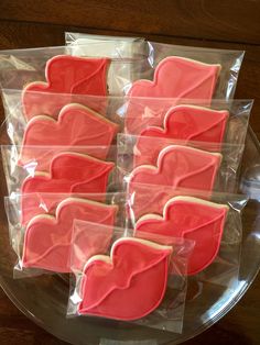 pink and white heart shaped cookies in plastic bags on a clear plate with wooden table