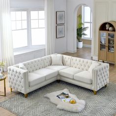 a white sectional couch sitting on top of a rug in a living room next to a window