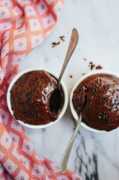 two white bowls filled with chocolate ice cream on top of a marble table next to a spoon