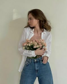 a woman is holding flowers in her hands and posing for the camera while leaning against a wall