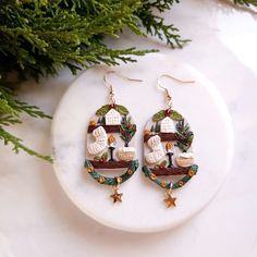 a pair of christmas themed earrings sitting on top of a white plate next to a pine tree