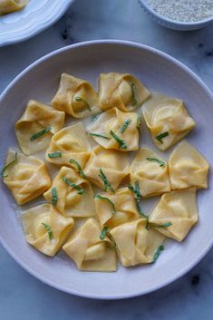 a white plate topped with ravioli next to two bowls filled with rice and seasoning