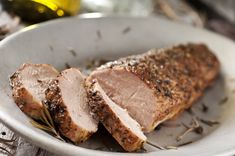 a white plate topped with meat covered in seasoning next to an olive oil bottle